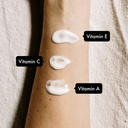 Close-up of arm with three white cream samples, labeled Vitamin E, Vitamin C, and Vitamin A, demonstrating key skincare ingredients