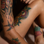 Close-up of colorful traditional-style tattoos on arm and torso, featuring a bird and floral designs