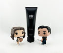 S1N Care body lotion bottle flanked by Funko Pop-style figurines representing the two founders - a female artist with palette and male golfer - illustrating the brand's diverse origins and appeal.